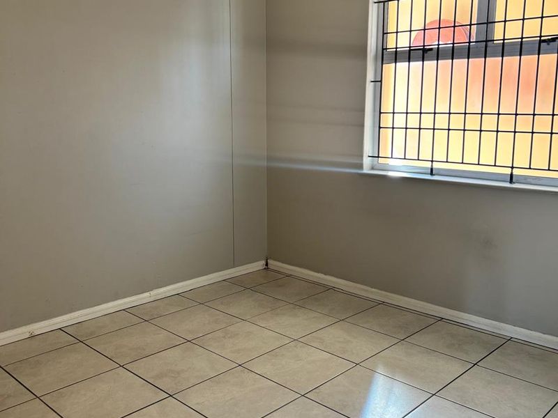 An empty bedroom featuring neutral tiled flooring, security bars on the window, and simple wall finishes, ready for personalization.