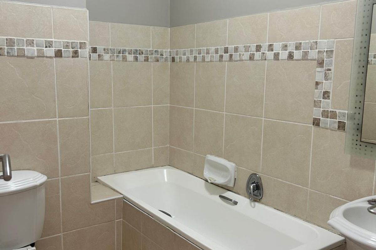 A functional bathroom featuring a built-in bathtub, pedestal washbasin, and neutral ceramic tiling throughout.