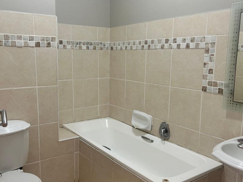 A functional bathroom featuring a built-in bathtub, pedestal washbasin, and neutral ceramic tiling throughout.
