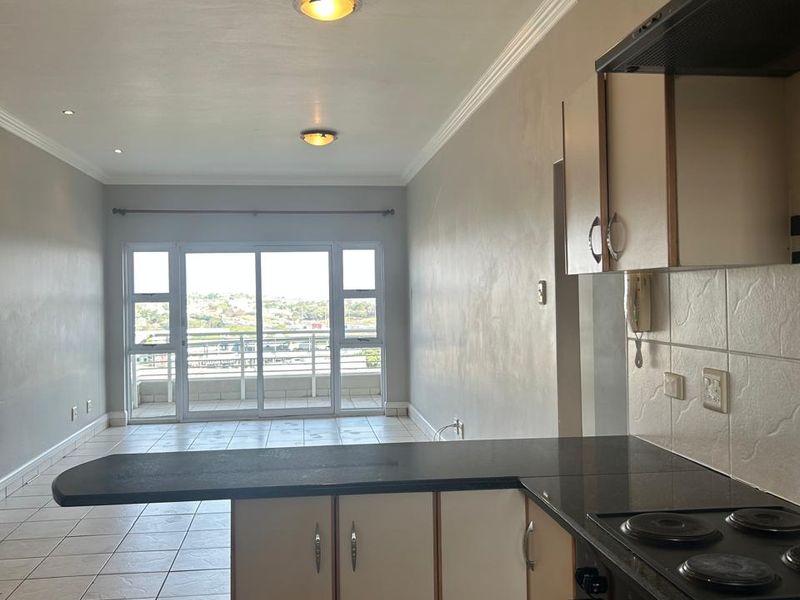 Open-plan kitchen and living area featuring tiled floors, built-in cabinetry with granite countertops, and sliding doors leading to a balcony with views.
