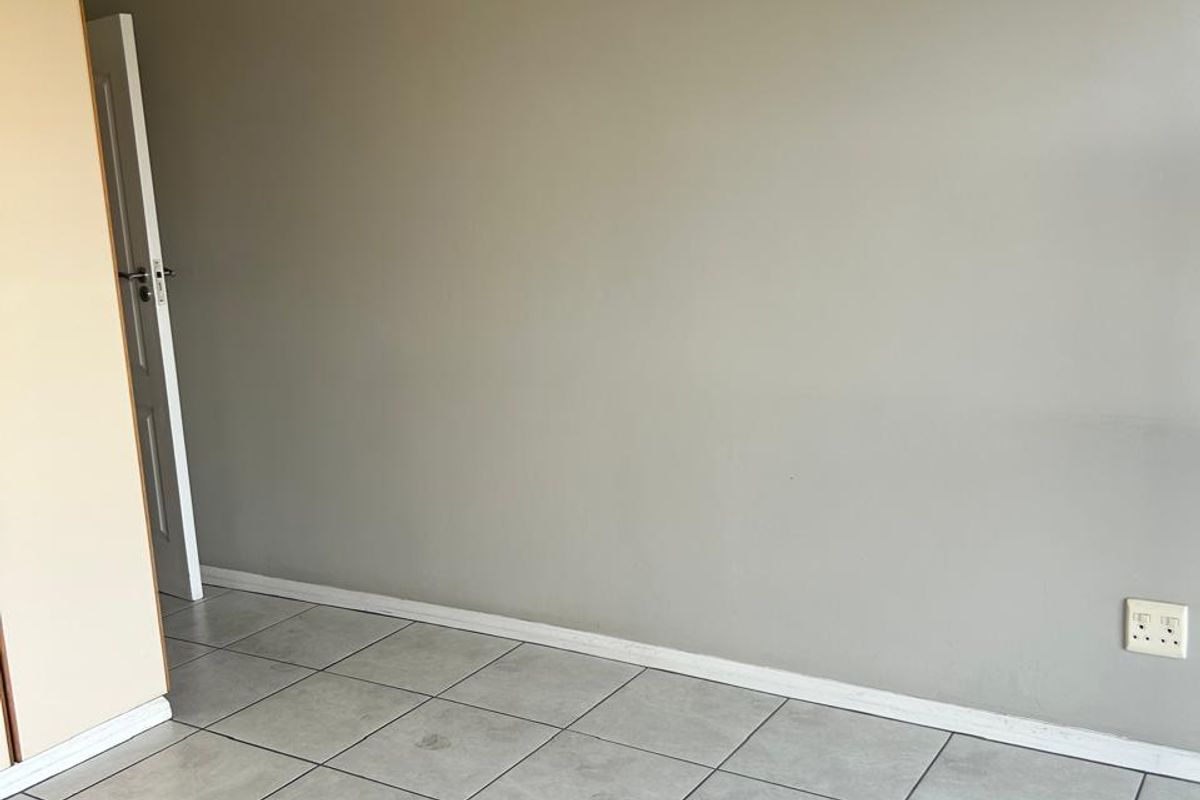 An empty bedroom featuring neutral grey walls, tiled flooring, and a built-in cupboard, providing a clean and versatile space.