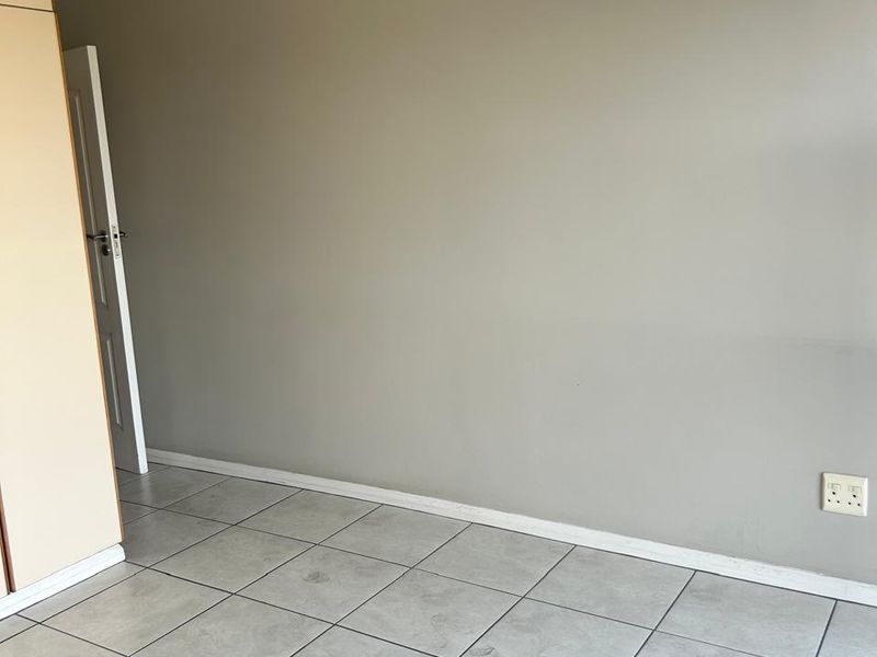 An empty bedroom featuring neutral grey walls, tiled flooring, and a built-in cupboard, providing a clean and versatile space.