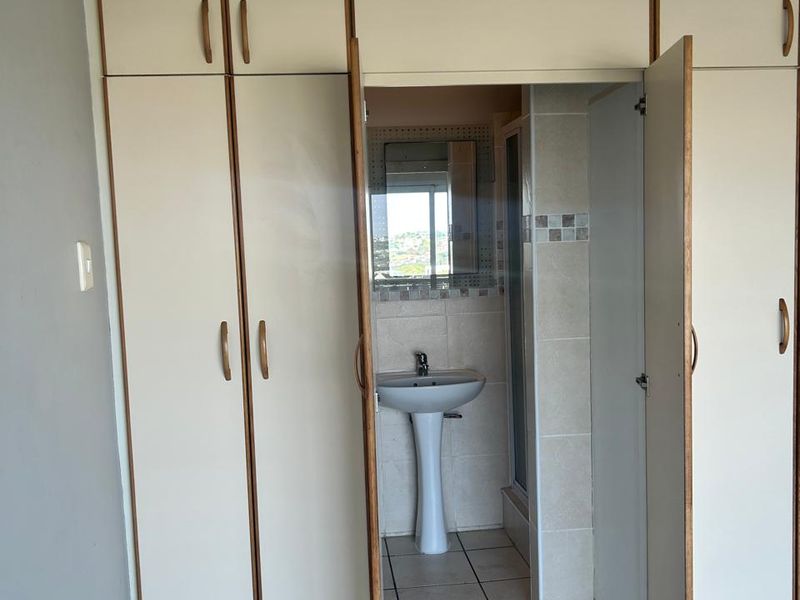 Bedroom featuring extensive built-in cupboards and an integrated en-suite bathroom with a pedestal basin and shower enclosure.