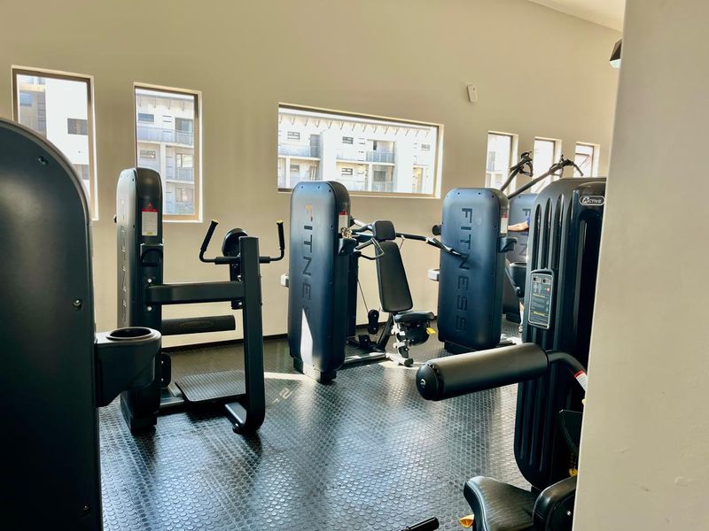 A well-maintained apartment complex gym featuring durable rubberized flooring and multiple windows providing natural light.