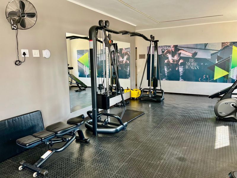 A functional home gym space featuring durable rubberized flooring, a large wall-mounted mirror, and a wall-mounted fan for ventilation.