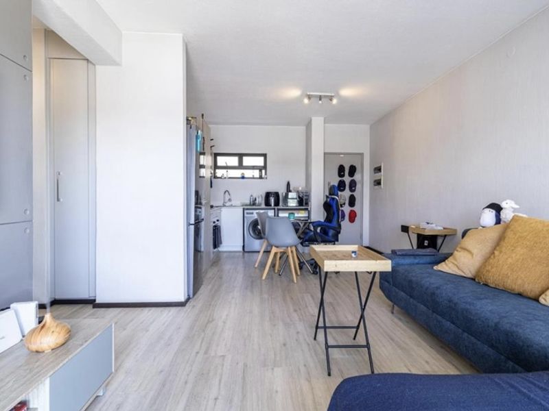 An open-plan living and kitchen area featuring light laminate flooring, neutral walls, and functional built-in cabinetry with integrated kitchen fixtures.