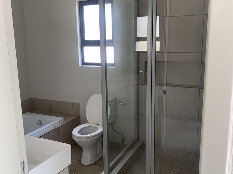 A functional bathroom featuring a built-in bathtub, separate shower enclosure, toilet, and vanity basin with neutral tiled finishes.
