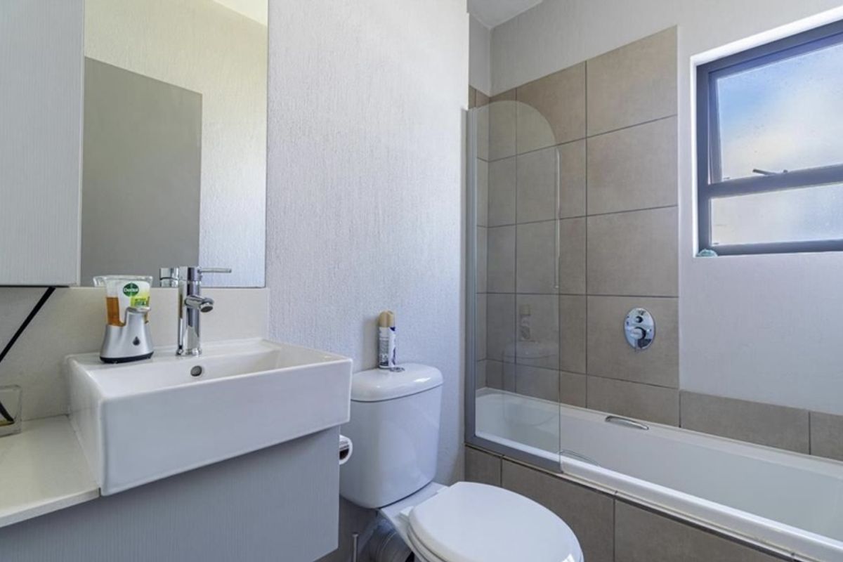 A modern bathroom featuring a vessel sink, a bathtub with a glass shower screen, and neutral wall tiling.