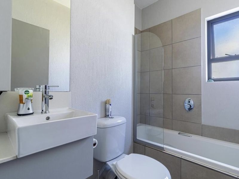 A modern bathroom featuring a vessel sink, a bathtub with a glass shower screen, and neutral wall tiling.