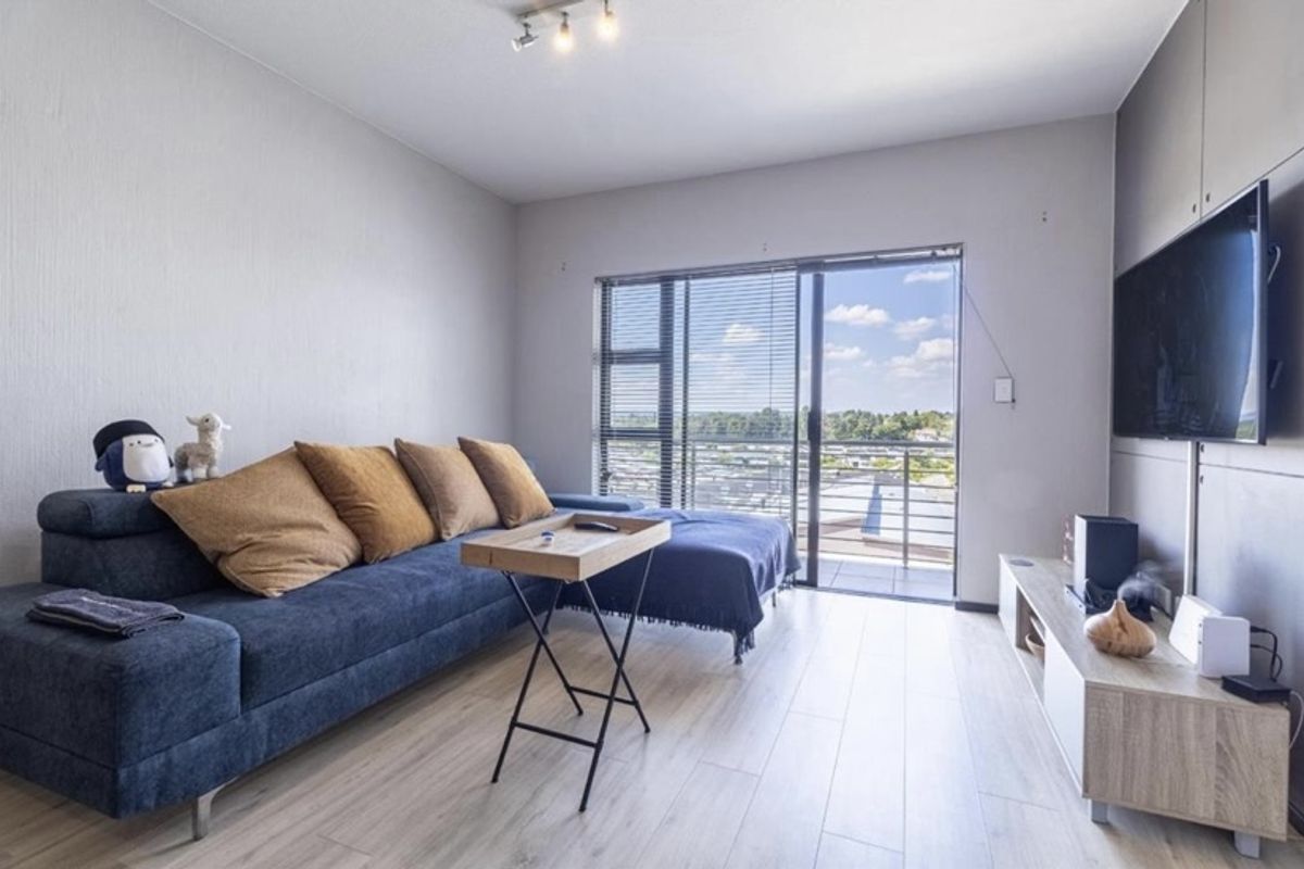 Modern living room featuring light laminate flooring, neutral walls, and a large sliding glass door providing access to a balcony with scenic views.