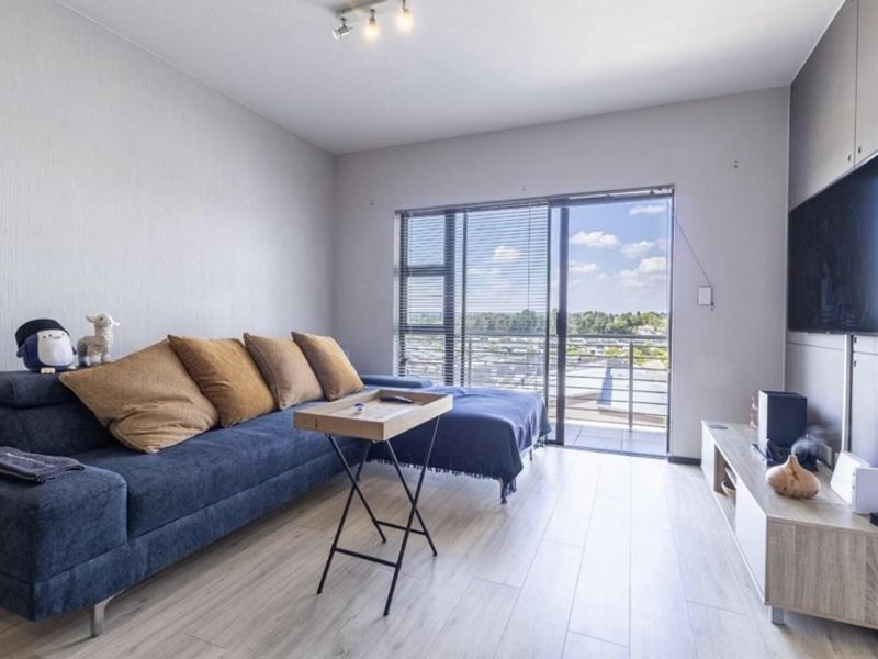 Modern living room featuring light laminate flooring, neutral walls, and a large sliding glass door providing access to a balcony with scenic views.