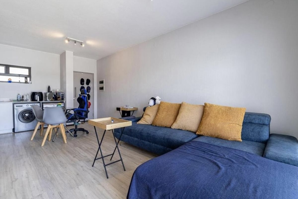 Open-plan living area featuring light laminate flooring and a compact kitchen corner with built-in cabinetry and sink.