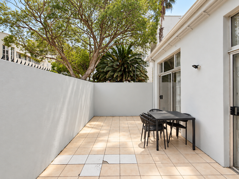 A private outdoor patio area featuring tiled flooring, perimeter walls, and direct access to the interior through sliding glass doors with security gates.