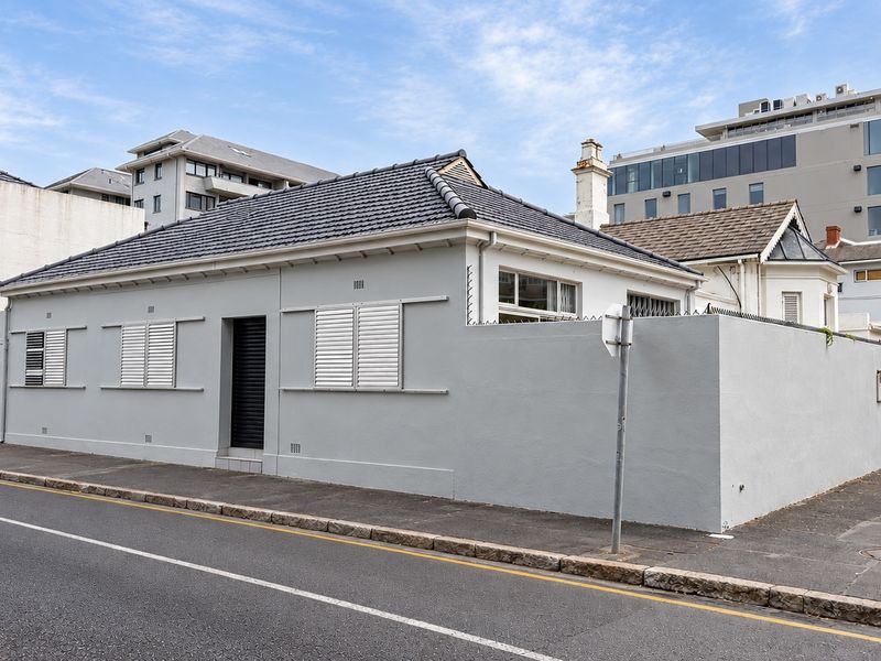 Street-facing view of a well-maintained single-story house featuring a tiled roof, secure perimeter wall, and white window shutters.