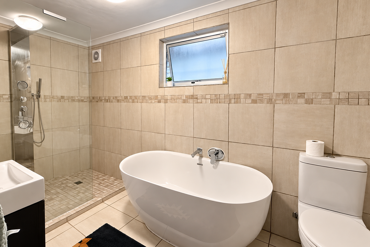 Modern bathroom featuring a freestanding bathtub, a spacious walk-in shower with glass enclosure, vanity basin, and neutral floor-to-ceiling tiling.