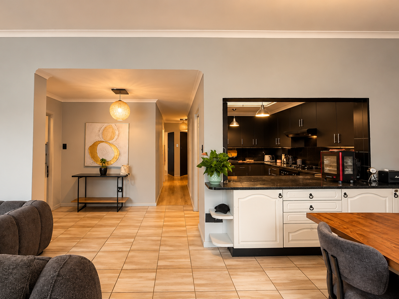Open plan living area featuring a kitchen with dark cabinetry, stone countertops, and a breakfast bar, flowing into a hallway and dining space.