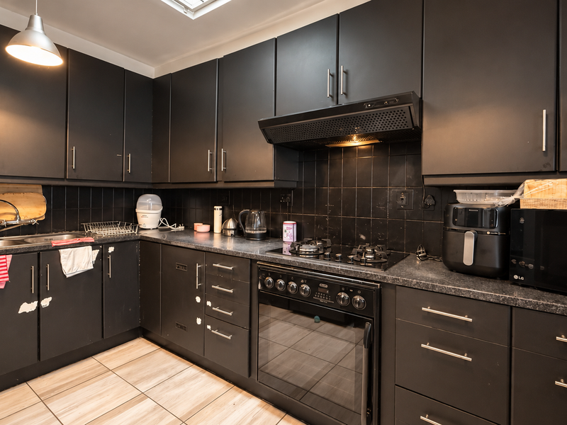 A functional kitchen featuring dark cabinetry, a gas cooktop, built-in oven, extractor fan, and tiled backsplash with neutral floor tiles.