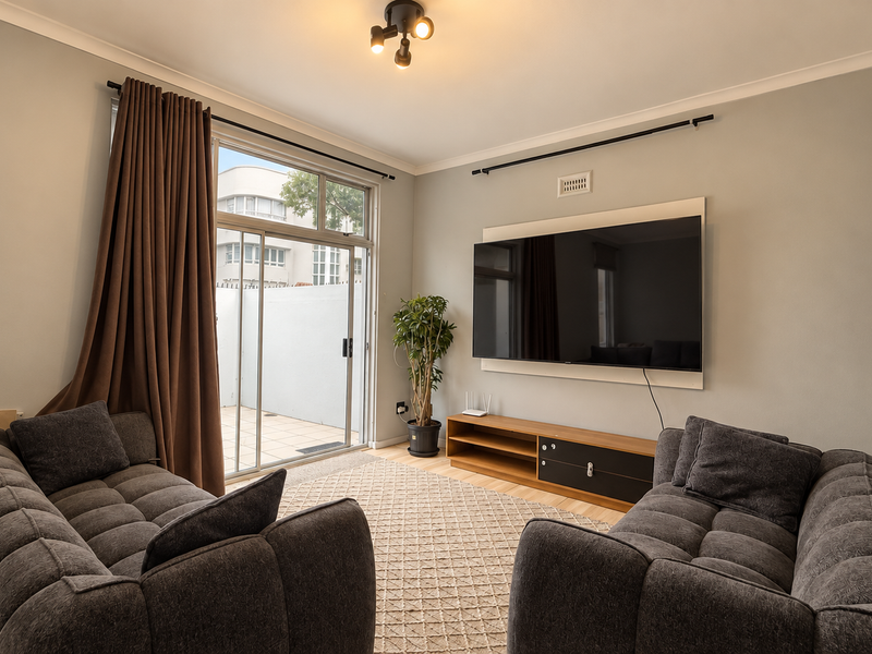 A well-maintained living room featuring a wall-mounted television unit, neutral wall finishes, and a large sliding glass door providing access to an outdoor patio area.