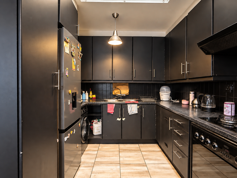 A modern kitchen featuring matte black cabinetry, a gas hob with extractor fan, built-in oven, and tiled backsplash with neutral floor tiles.