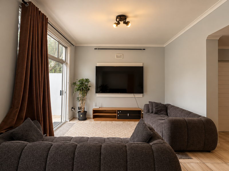 A well-maintained living room featuring tiled flooring, a sliding glass door providing natural light, and a modern ceiling light fixture.