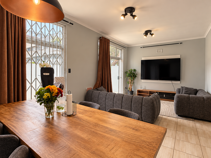 Spacious open-plan living and dining area featuring tiled floors, modern lighting, and a wall-mounted television, with direct access to the exterior through sliding doors.
