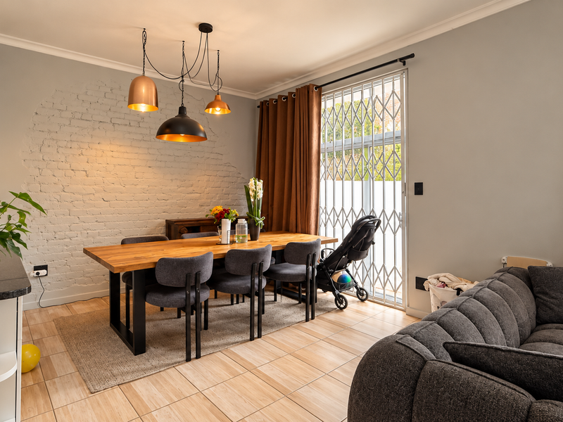 Open-plan living and dining area featuring an exposed brick accent wall, tiled flooring, and direct access to the exterior through a security gate.