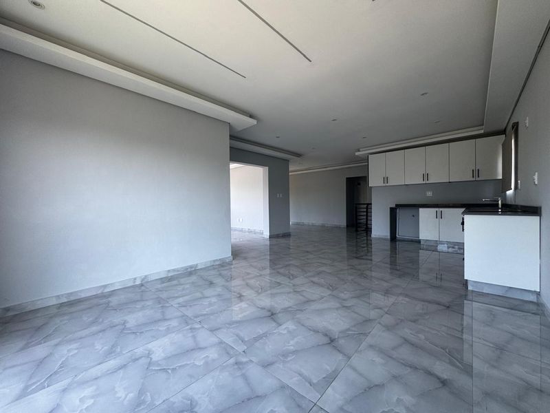 Spacious open-plan living and kitchen area featuring modern grey marble-look floor tiles, neutral walls, and contemporary built-in cabinetry with stone countertops.