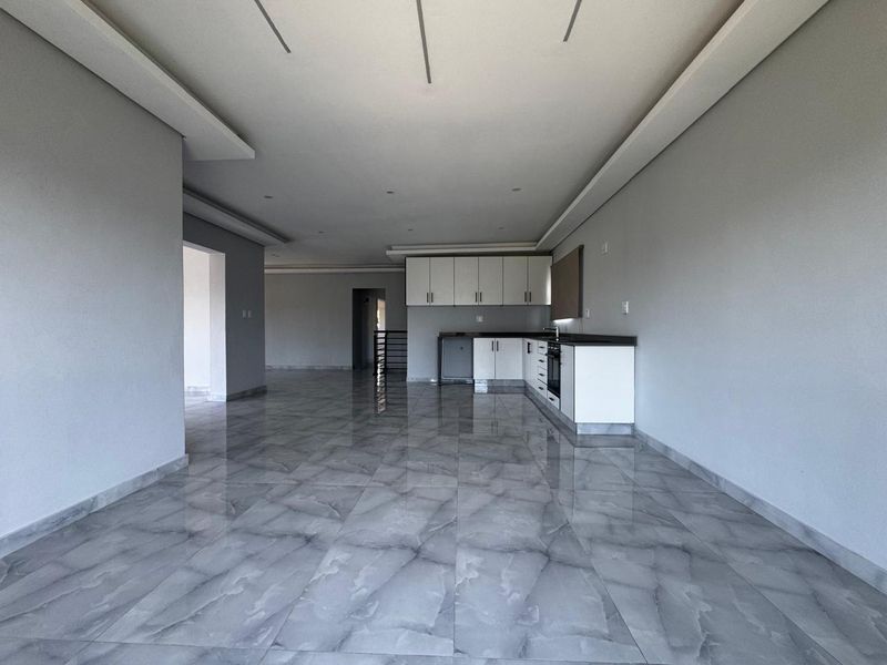 Spacious open-plan living area featuring modern tiled flooring, recessed ceiling lighting, and a sleek, minimalist kitchen with built-in cabinetry and integrated appliances.