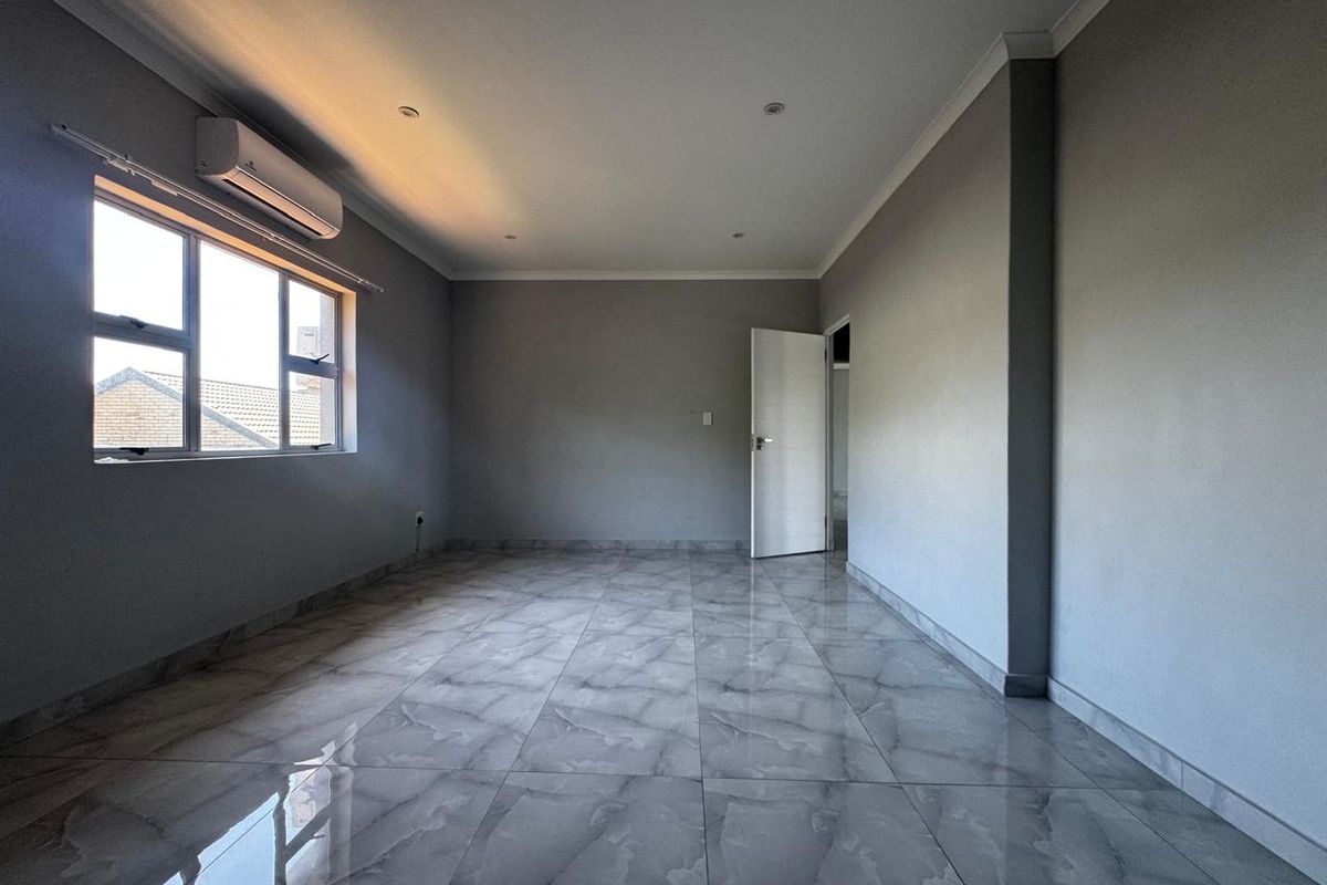 A spacious, empty bedroom featuring modern grey tiled flooring, recessed downlighting, and a wall-mounted air conditioning unit.