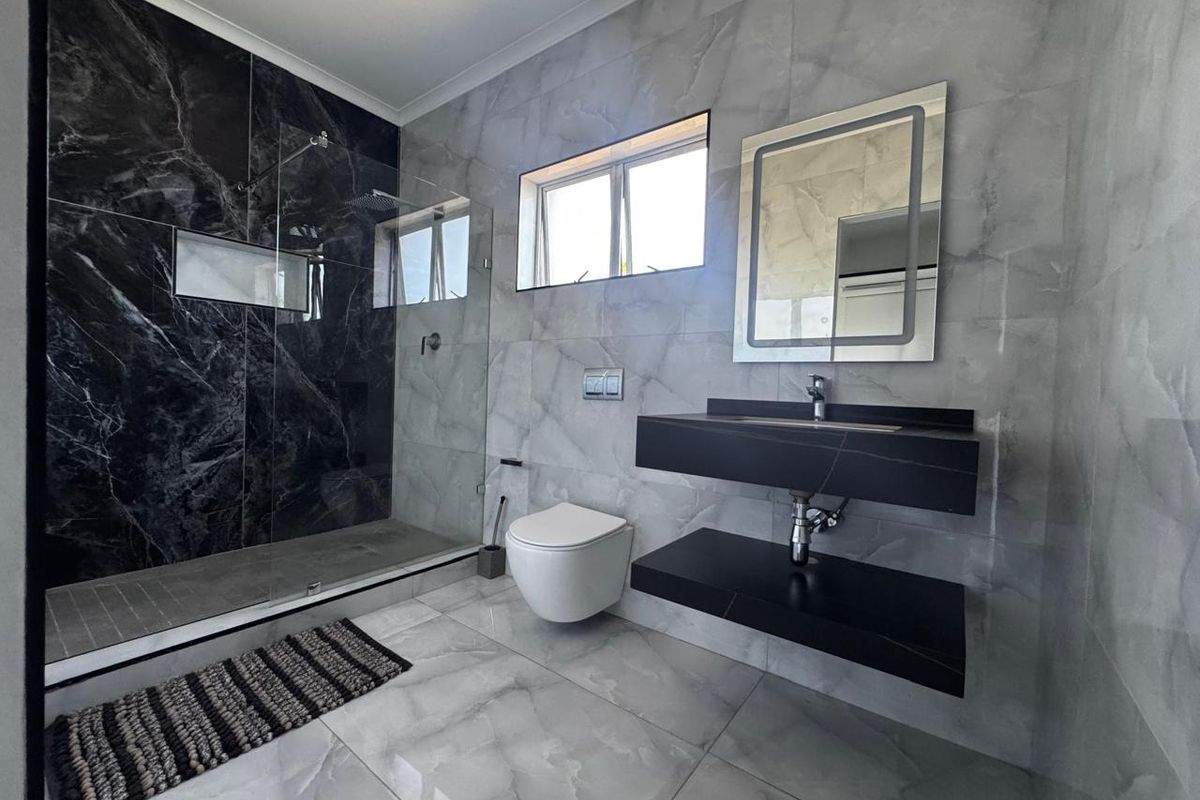 Modern bathroom featuring a walk-in shower with dark marble-effect tiling, a wall-mounted toilet, and a sleek floating vanity with an integrated basin.