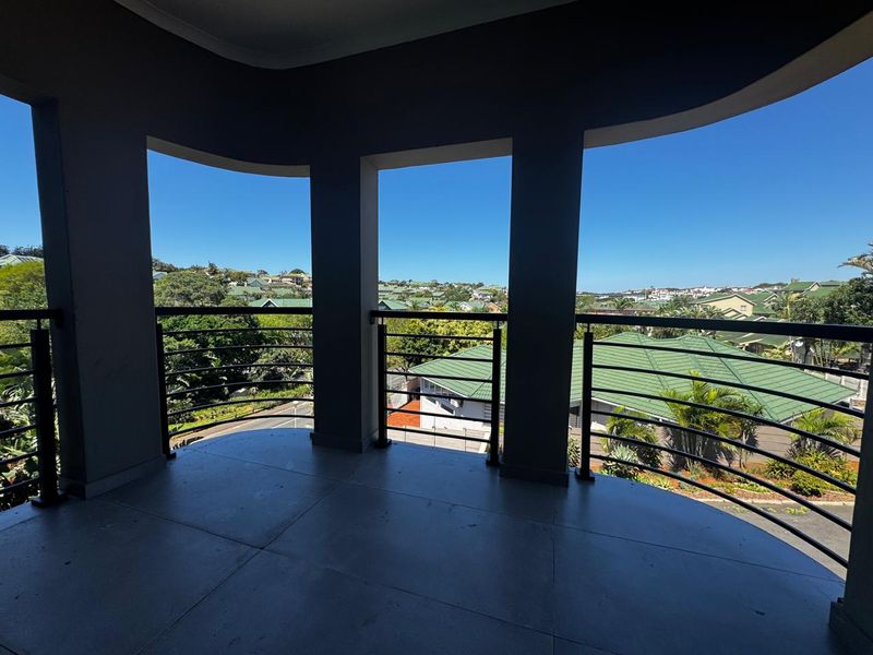 A spacious covered balcony featuring tiled flooring and a metal balustrade, offering elevated views of the surrounding neighborhood.