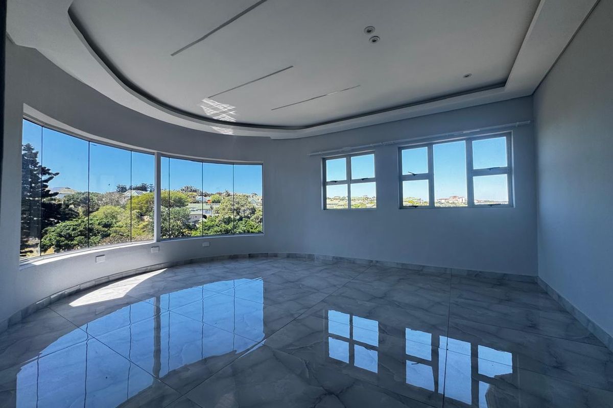 A bright, spacious living area featuring polished porcelain tiles, a modern recessed ceiling tray, and expansive curved windows offering panoramic views.