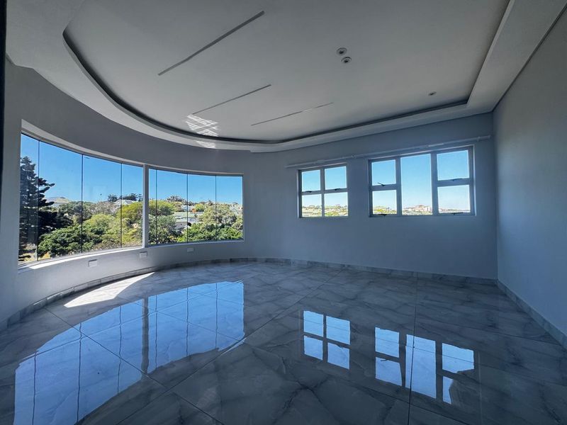 A bright, spacious living area featuring polished porcelain tiles, a modern recessed ceiling tray, and expansive curved windows offering panoramic views.