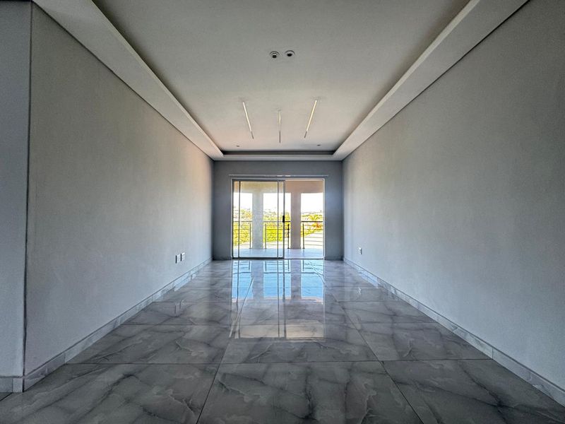 A bright, empty living room featuring modern recessed ceiling lighting, polished porcelain tile flooring, and a sliding glass door leading to an outdoor balcony.
