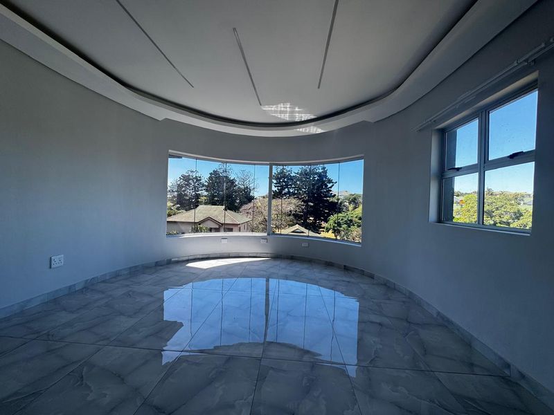 A bright, empty living area featuring large curved windows, modern tiled flooring, and a decorative recessed ceiling design.