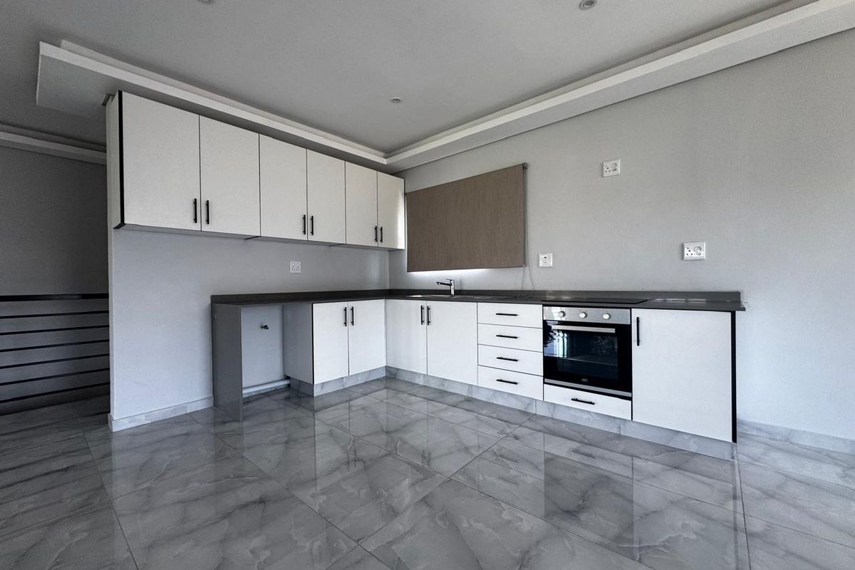 Modern kitchen featuring white cabinetry, dark stone countertops, integrated oven, and sleek grey tiled flooring in a clean, minimalist space.