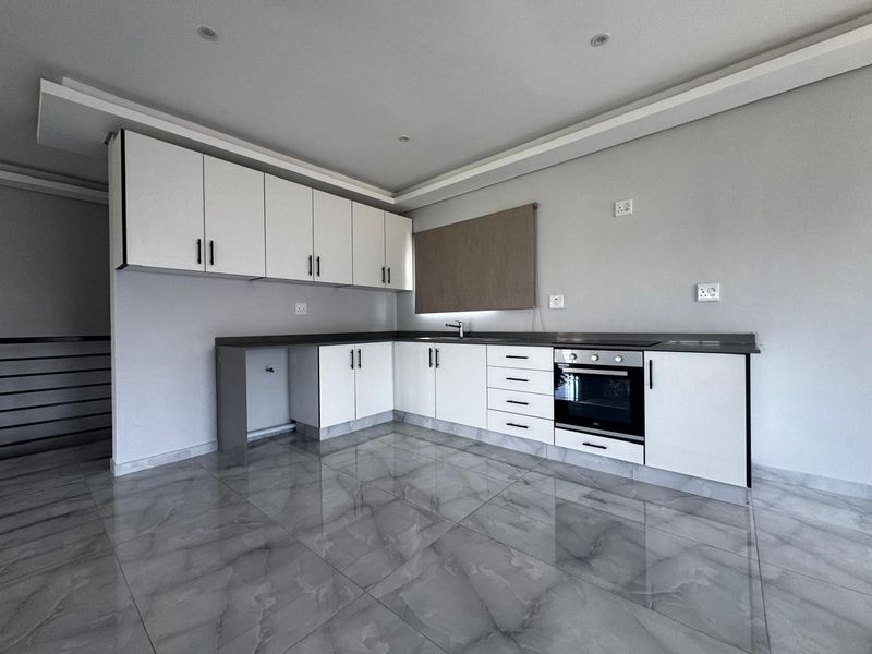 Modern kitchen featuring white cabinetry, dark stone countertops, integrated oven, and sleek grey tiled flooring in a clean, minimalist space.