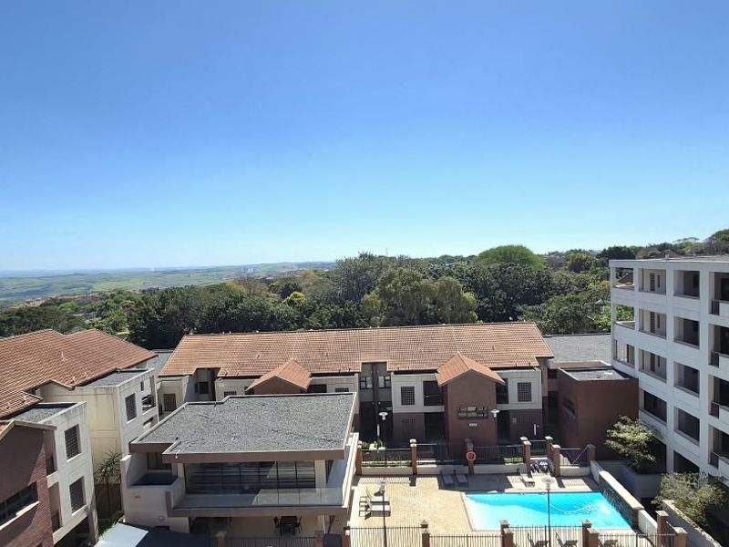 Elevated view overlooking the apartment complex, featuring a communal swimming pool, landscaped surroundings, and distant horizon views.