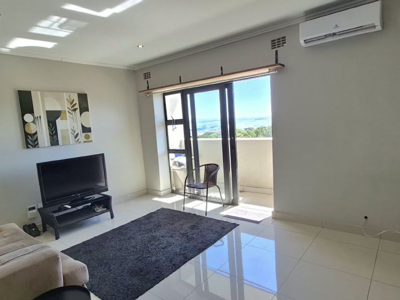 A bright living room featuring tiled flooring, recessed lighting, and an air conditioning unit, with direct access to a balcony through sliding glass doors.
