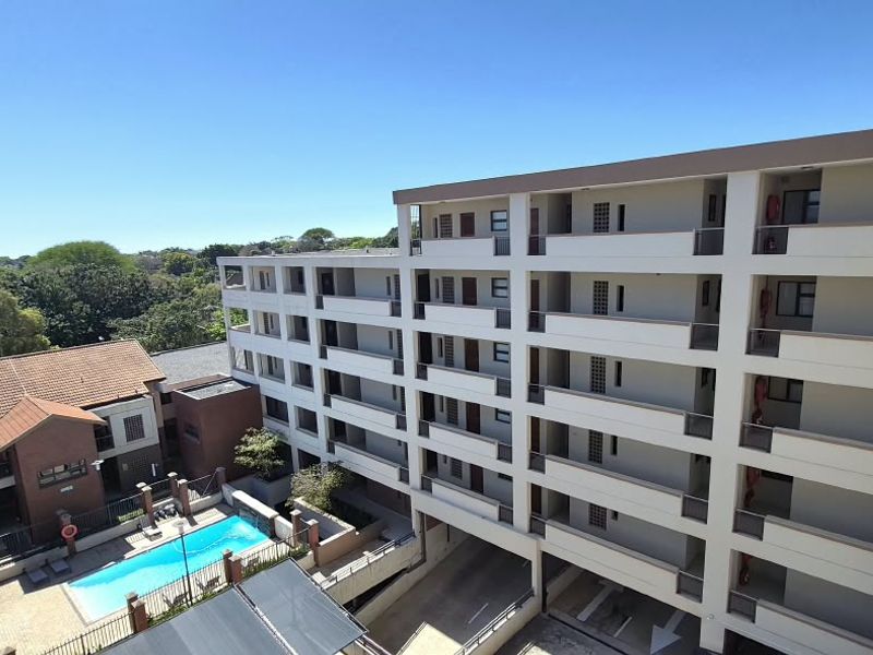 Aerial view of the apartment complex featuring a swimming pool, multi-level balconies, and ground-level parking facilities.