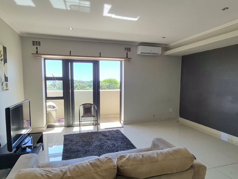 Spacious living room featuring tiled floors, a dark accent wall, air conditioning, and a sliding glass door leading to a balcony.