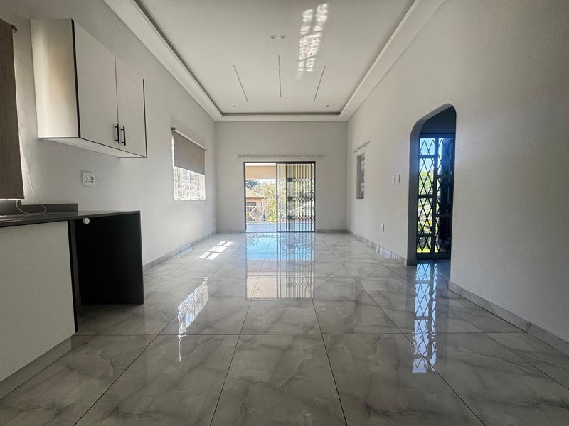 Spacious open-plan living area featuring polished porcelain tiles, modern coffered ceilings with recessed lighting, and direct access to an outdoor patio.