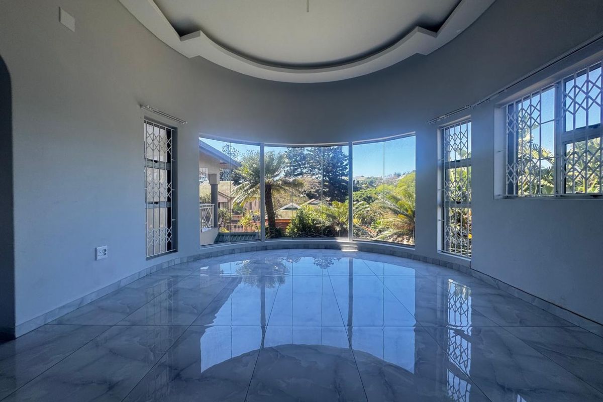 Spacious living area featuring polished porcelain tiles, a decorative recessed ceiling, and large windows offering natural light and garden views.