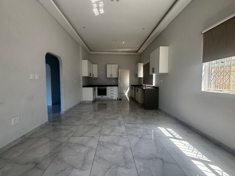 Spacious open-plan kitchen area featuring modern cabinetry, built-in oven, hob, and polished tiled flooring throughout, offering a clean and bright living space.