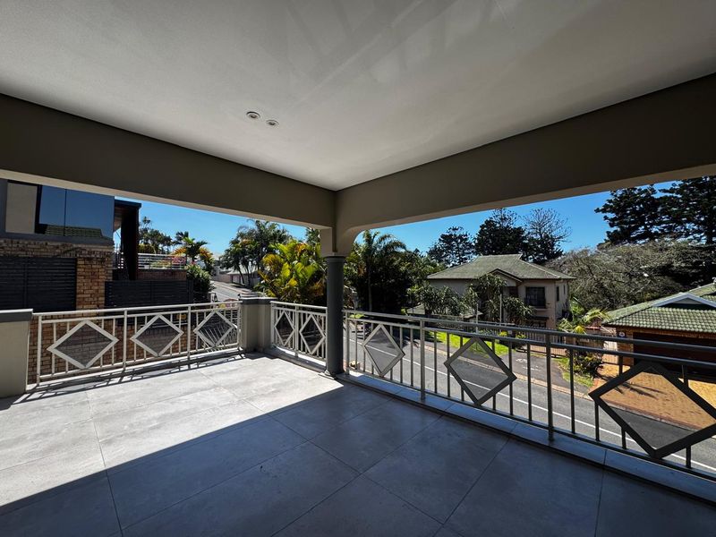 A spacious covered balcony featuring modern tiled flooring and a decorative metal balustrade, offering an elevated view of the surrounding neighbourhood.