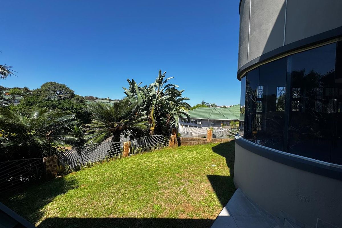 A view of the rear garden featuring a curved architectural window, manicured lawn, and secure boundary walling with metal fencing.
