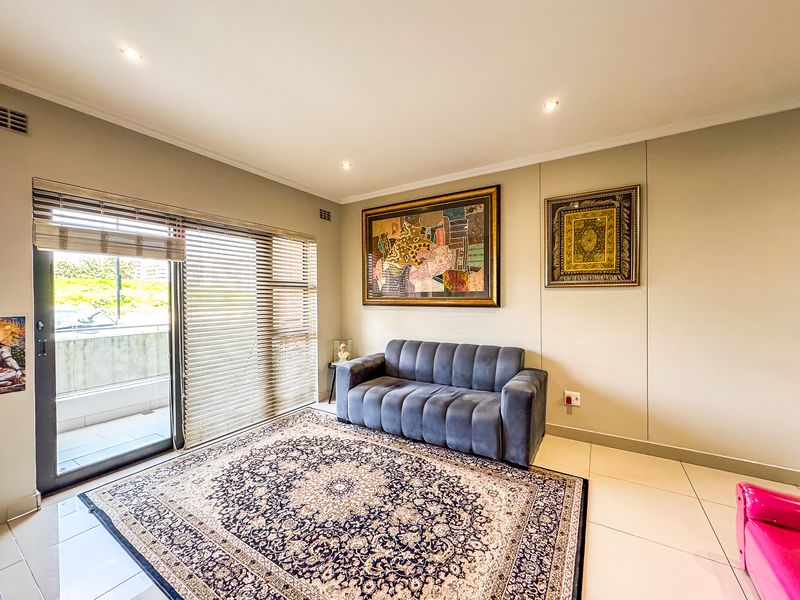 A bright living room featuring large sliding glass doors with venetian blinds, recessed downlighting, and neutral tiled flooring.