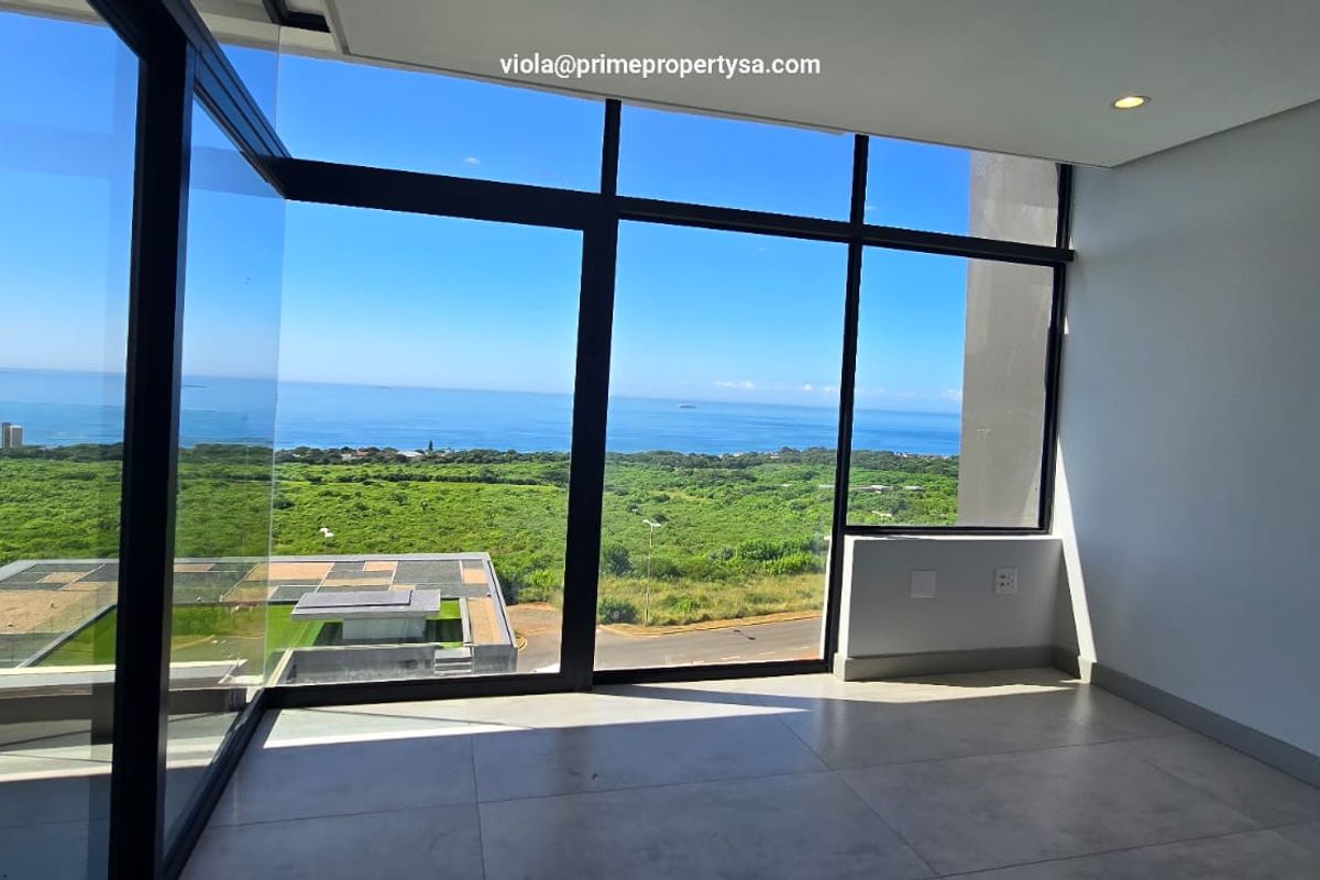 A bright, empty living area featuring expansive floor-to-ceiling windows with panoramic ocean and landscape views, finished with modern neutral floor tiles.