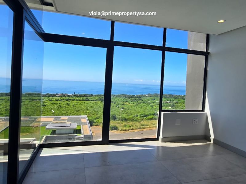 A bright, empty living area featuring expansive floor-to-ceiling windows with panoramic ocean and landscape views, finished with modern neutral floor tiles.