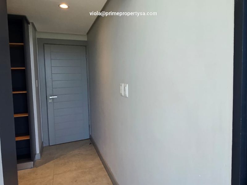 A clean, modern hallway featuring neutral tiled flooring, recessed downlighting, and built-in shelving units.